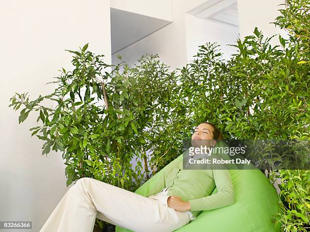 ビジネスウーマンにクッションの植物に囲まれています。 - ビーズソファ ストックフォトと画像