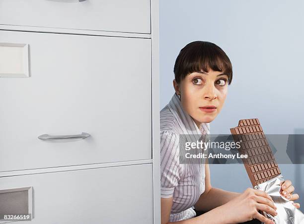 businesswoman hiding and eating chocolate bar - candy bar stock-fotos und bilder