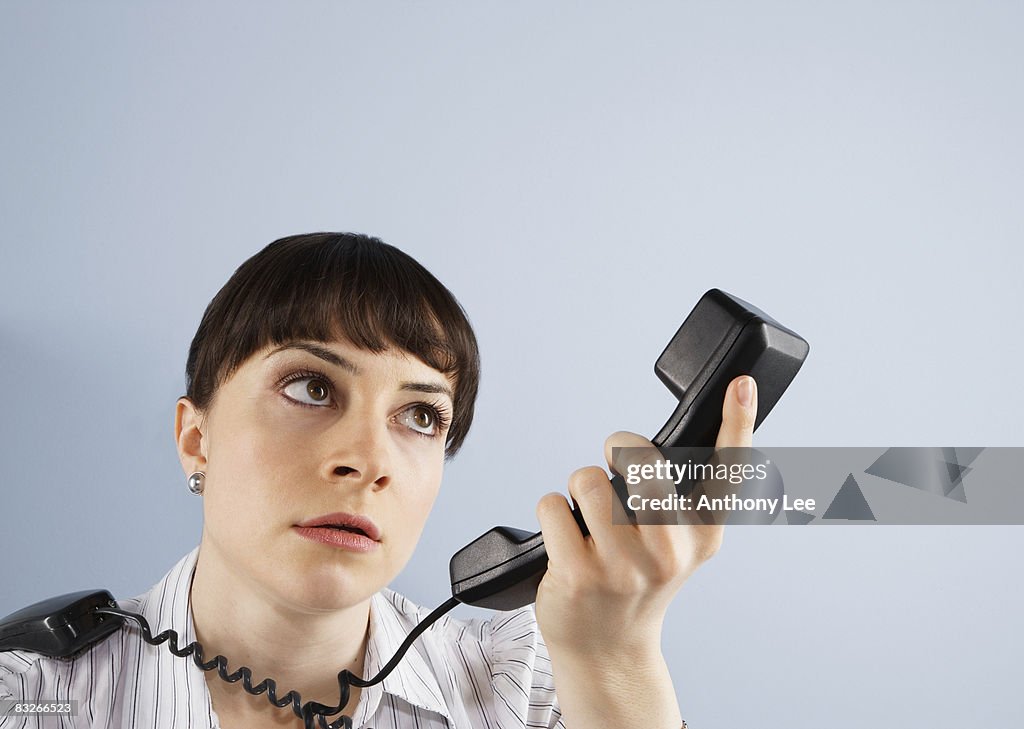 Frustrated businesswoman looking at telephone handset