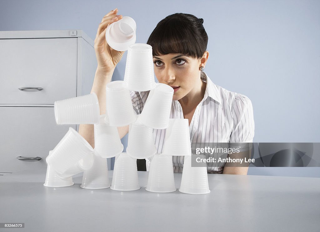 Businesswoman stacking plastic cups into pyramid