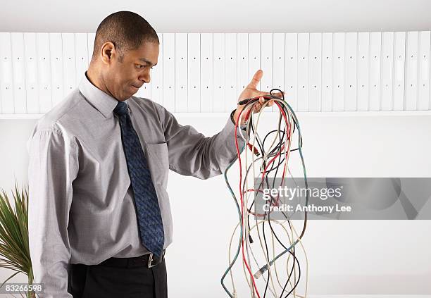 businessman examining a tangle of electronic cords - tangled stockfoto's en -beelden