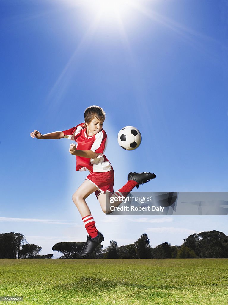 Young boy in uniform kicking soccer ball