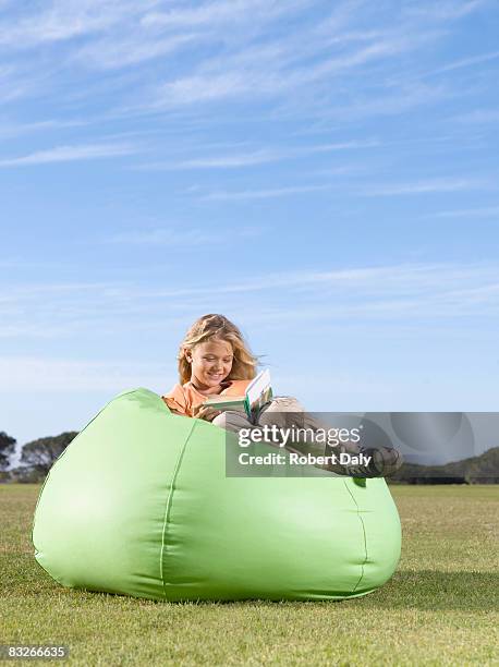 young girl in bean bag reading outdoors - bean bags stock pictures, royalty-free photos & images