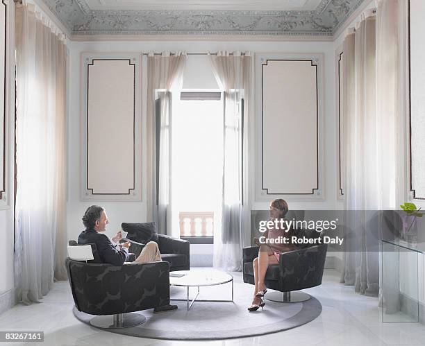 couple drinking coffee in sitting room - woman elegant crossed legs stockfoto's en -beelden
