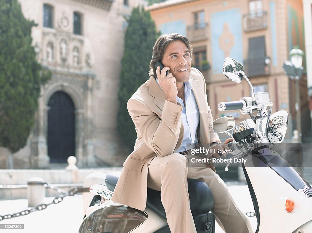 Uomo d'affari seduto su uno scooter e parlare sul telefono cellulare