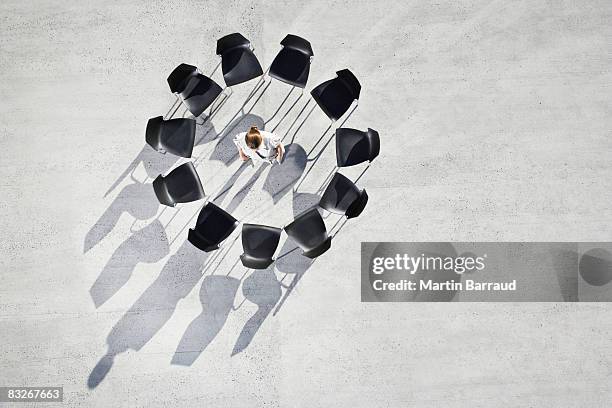 businesswoman standing in center of circle of office chairs - standing on chair stockfoto's en -beelden