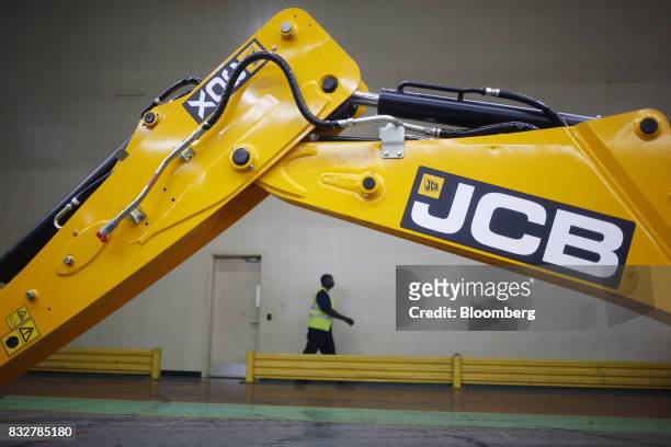 Worker passes in front of a backhoe loader construction vehicle at the JC Bamford Excavators LTD. Manufacturing plant in Pooler, Georgia, U.S., on...