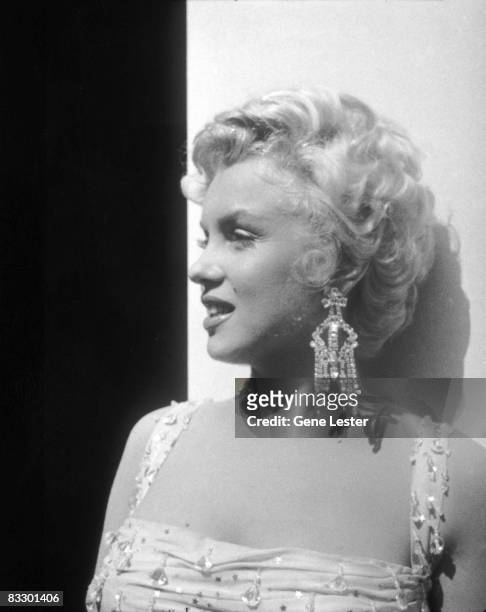 Portrait of American actor Marilyn Monroe , in a light-colored, beaded gown, as she leans against an open trailer door on the 20th Century Fox...
