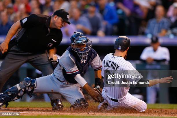 Jonathan Lucroy of the Colorado Rockies slides safely under the tag of catcher Kurt Suzuki of the Atlanta Braves as home plate umpire Dan Bellino...