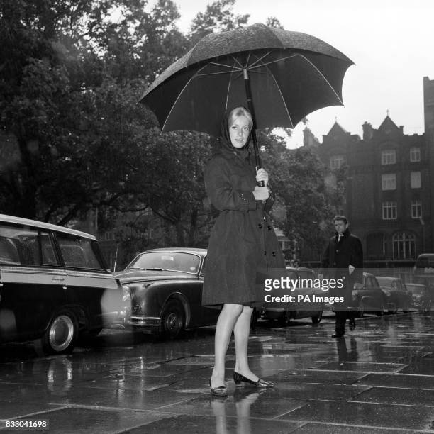 Catherine Deneuve, French actress using an umbrella as she left her London hotel to go to work on the film Repulsion.