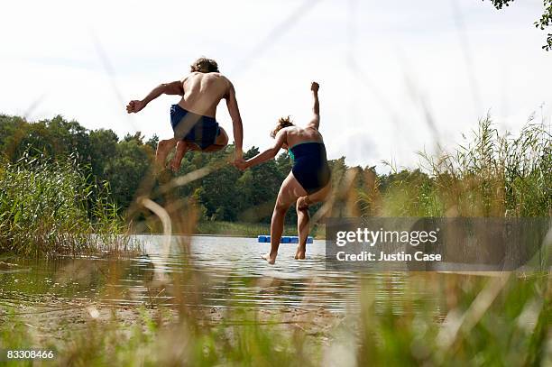 couple jumping into the air by edge of lake - tiener koppel stockfoto's en -beelden