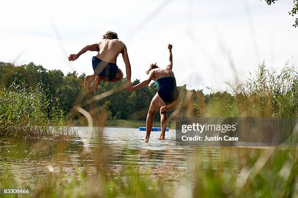 couple jumping into the air by edge of lake - air date stockfoto's en -beelden