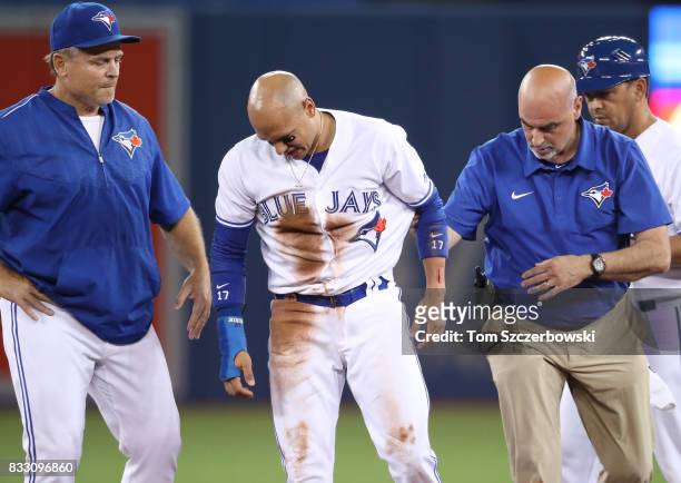 Ryan Goins of the Toronto Blue Jays exits the game with his arm bleeding with the assistance of trainer George Poulis and manager John Gibbons after...
