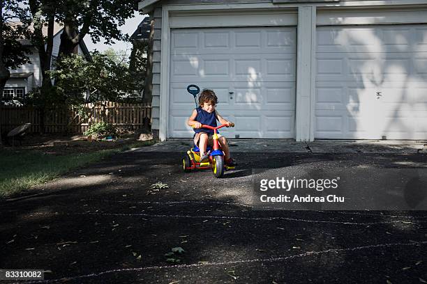 young boy racing down driveway on tricycle. - racing garage stock pictures, royalty-free photos & images