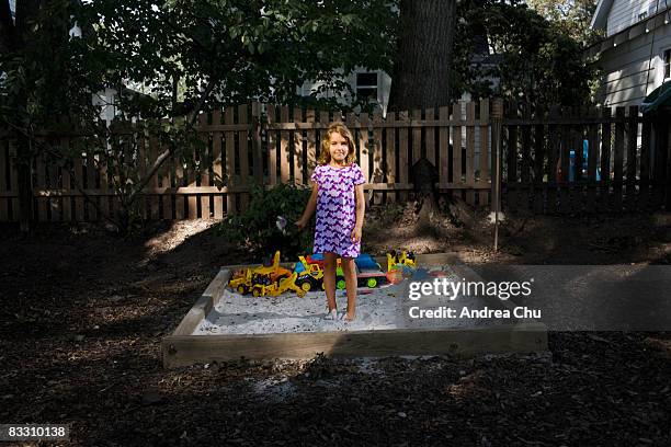 young girl standing in sandbox holding flowers. - solo bambine femmine foto e immagini stock