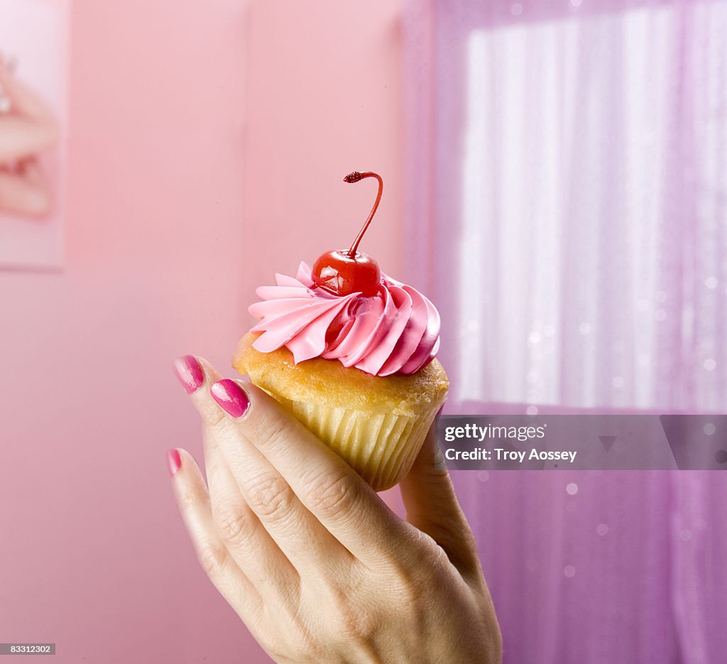 Hand holding cupcake with cheery in pink room