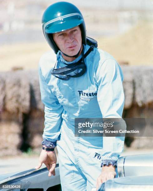 American actor Steve McQueen in Firestone racing driver suit near a Lola T70 SL70/14 car, at Riverside Raceway in Riverside, California, circa 1966.