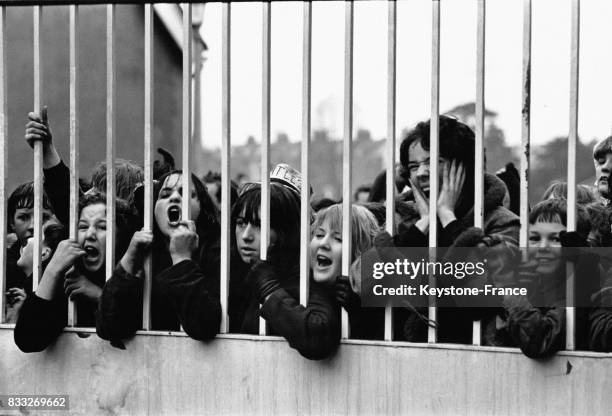 Jeunes groupies attendant les Beatles, sous la pluie, devant les grilles d'un studio, à Teddington, Royaume-Uni, le 24 février 1964.