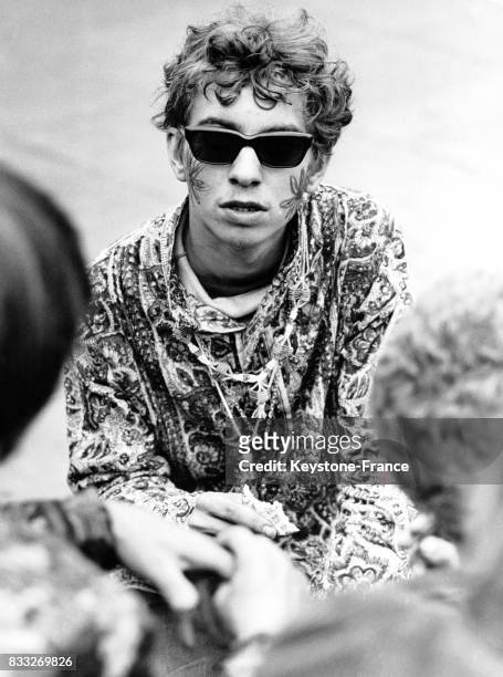 Portrait d'un jeune hippie avec des lunettes de soleil et des fleurs dessinées sur les joues, à Londres, Royaume-Uni, circa 1960.