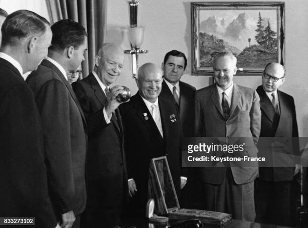Dans le bureau oval de la Maison-Blanche, le Président Eisenhower regarde une sphère miniature représentant la sonde spatiale Lunik 2 qu'il tient...