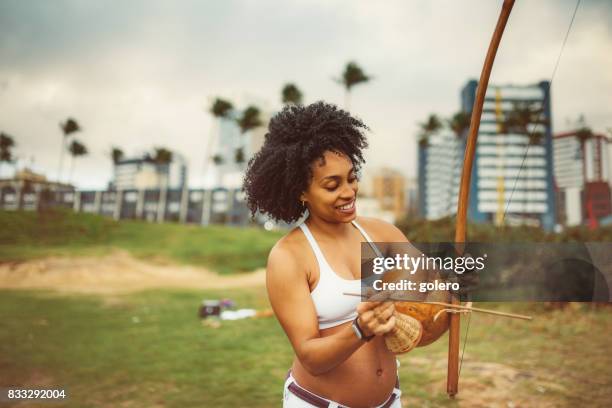 pregnant afro-brazilan woman playing berimbau at beach - berimbau stock pictures, royalty-free photos & images
