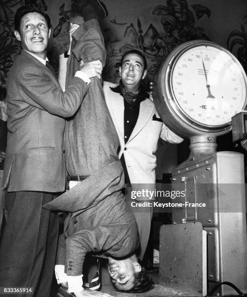 La gare des Invalides, François Périer est sur la bascule la tête en bas, tenu par les pieds par Jean Sablon, à Paris, France le 23 juillet 1950.