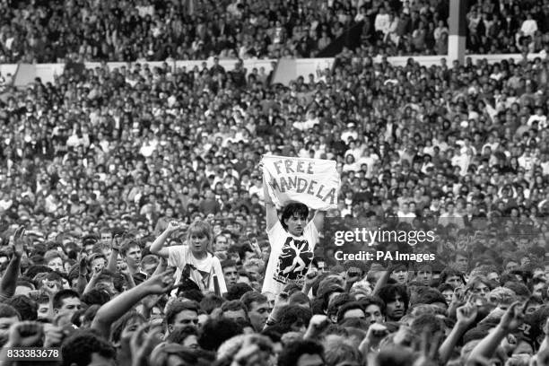 Member of the crowd holds up a banner saying "Free Mandela". Reference to Nelson Mandela's imprisonment in Robben Island