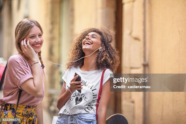 two young women friends having fun sharing music in the street - sharing headphones stock pictures, royalty-free photos & images