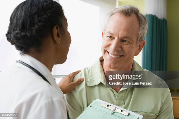 female doctor putting hand on male patient - 50 year old male patient stock pictures, royalty-free photos & images