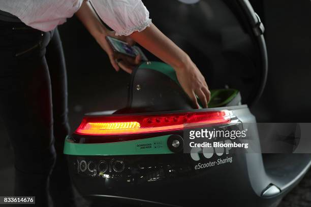 An employee stows a crash helmet in the underseat storage compartment of a Coup eScooter electric hire vehicle, operated by Robert Bosch GmbH, in...