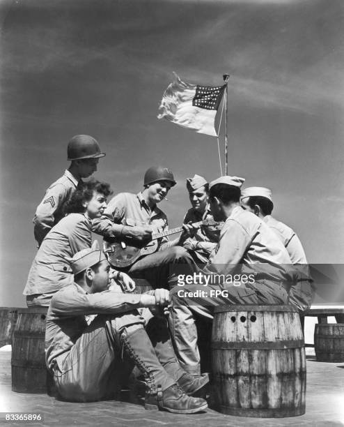 American servicemen listening to a guitar player on the roof of an American Red Cross beach club, known as the 'Paradise', in Ain El Turk District,...