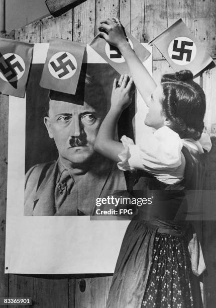 Young woman in the Sudetenland region of Czechoslovakia, places swastika flags around a portrait of Nazi leader Adolf Hitler in anticipation of the...