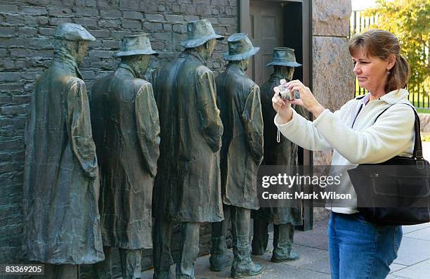 Tourist Terri Garren of Olympia, Washington, takes a picture near life size bronze statues depicting men standing in a line during the great...
