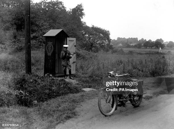 An AA emergency inspector uses an Automobile Association Roadside telephone box on Epsom Road in Surrey. His bike, a recent introduction to the AA,...