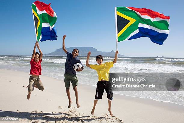 young boys on the beach with soccer ball and waving south african flag with table mountain in the background, cape town, western province, south africa - south african flag stock pictures, royalty-free photos & images