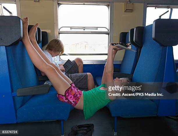 two kids reading on train, one with mp3 player - barefoot feet up lying down girl stockfoto's en -beelden
