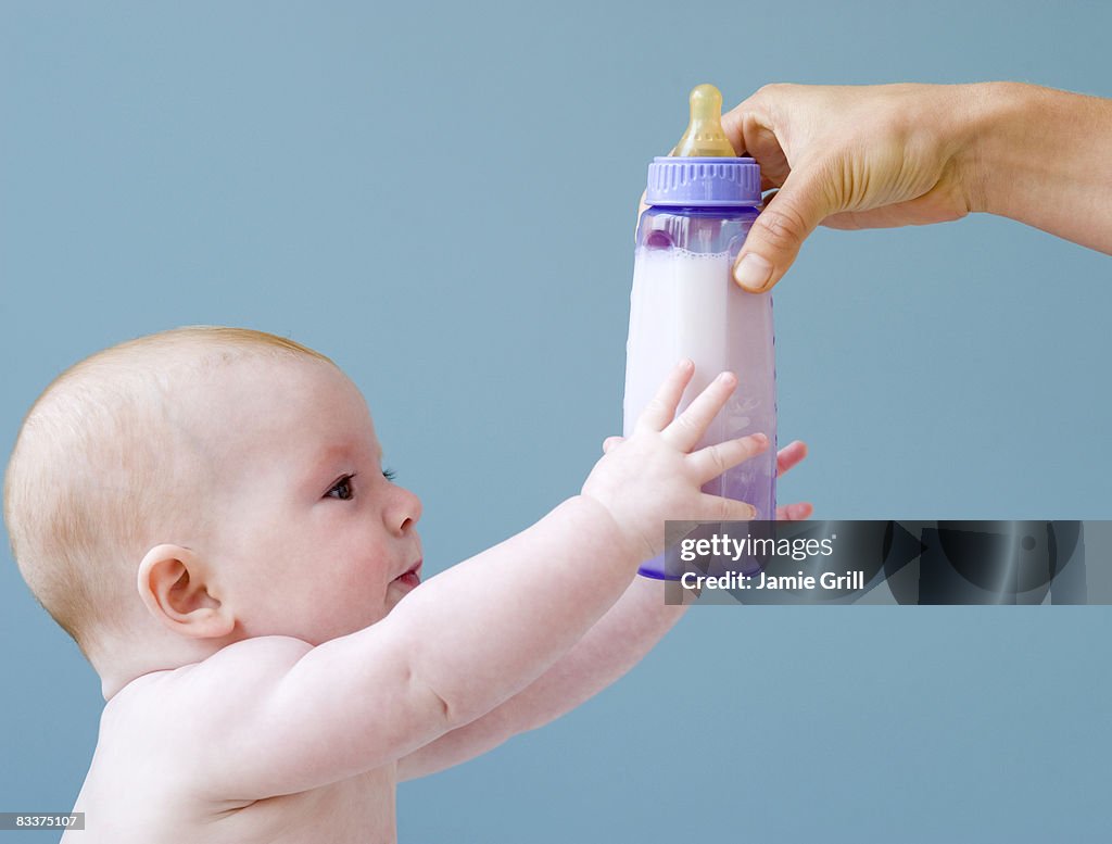 Baby reaching for bottle of milk from mother