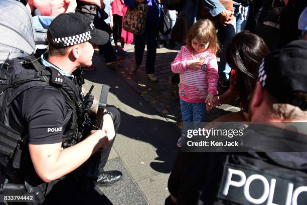 Armed police officers crouch down to chat to a young girl on the Royal Mile during the Edinburgh Festival Fringe where security has this year been...