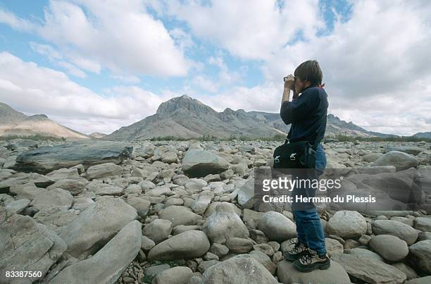 woman looking through binoculars on rocky river bed, pella, northern cape province, south africa - noorderlijke kaapprovincie stockfoto's en -beelden