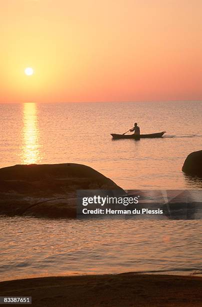 silhouette of man in dug-out canoe against the setting sun, senga bay, malawi - dugout canoe fotografías e imágenes de stock