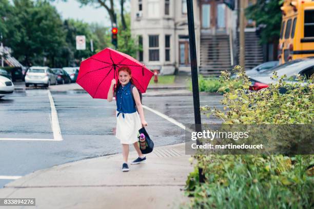 young redhead girl under red umbrella walking to school. - montreal street stock pictures, royalty-free photos & images