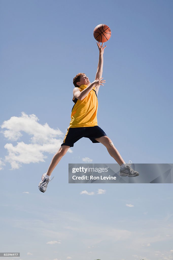 Boy playing basketball, airborne