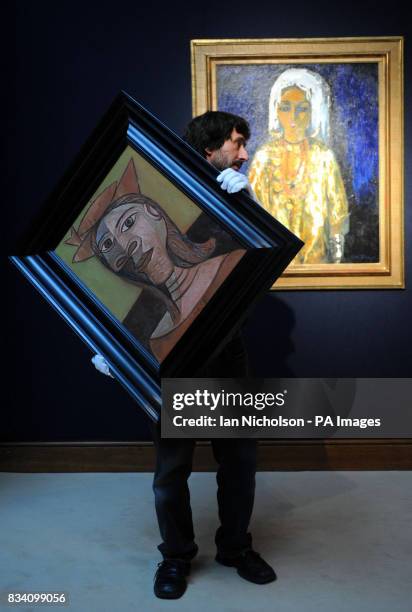 Porter at Christie's auctioneers carries Pablo Picasso's Femme au chapeau past L'Ouled Nail, by Kees Van Dongen, at a preview of works of art which...