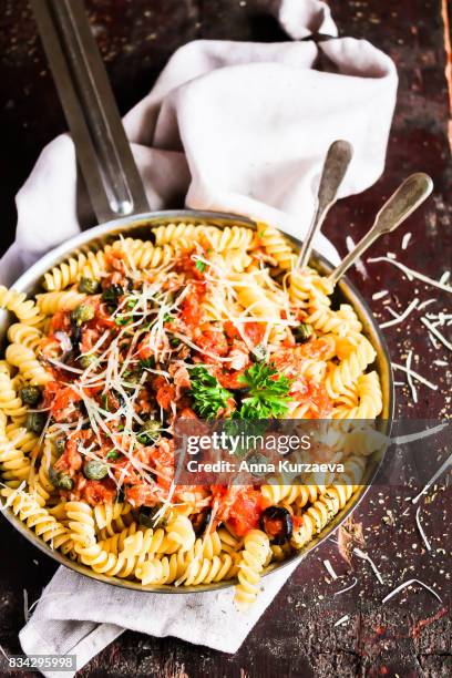 fusilli pasta dish with tuna fish, tomato sauce, capers, black olives and parmesan cheese in a cooking pan on a wooden table, selective focus - tomato sauce stock pictures, royalty-free photos & images