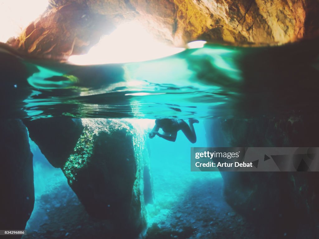 Girl doing snorkel exploring the natural cave in the shoreline of Costa Brava Mediterranean Sea during summer vacations in a paradise place taking picture with dome cover and underwater view.