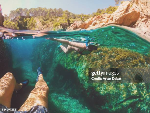 couple doing snorkel exploring the natural cave in the shoreline of costa brava mediterranean sea during summer vacations in a paradise place taking picture with dome cover and underwater view. - romance cover stock pictures, royalty-free photos & images