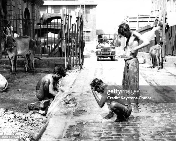 Des hommes se lavent dans le caniveau avec l'eau non pure sortant d'une canalisation, à Calcutta, Inde en mars 1963.