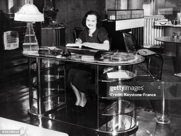 Jeune femme assise à un bureau transparent fait en verre et commandé par un prince hindou, en 1937.