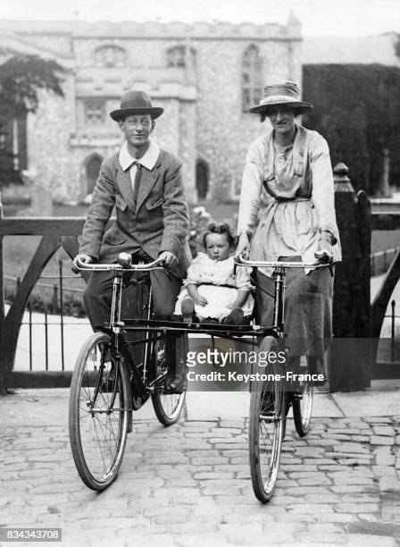 Ces parents présentent leur invention, une poussette pour leur bébé entre leur deux vélos, auu Royaume-Uni.