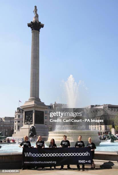 Campaigners hold a banner subtitling the 'whoosh' of the fountain to highlight Deaf Awareness Week by subtitling major landmarks, Trafalgar Square,...